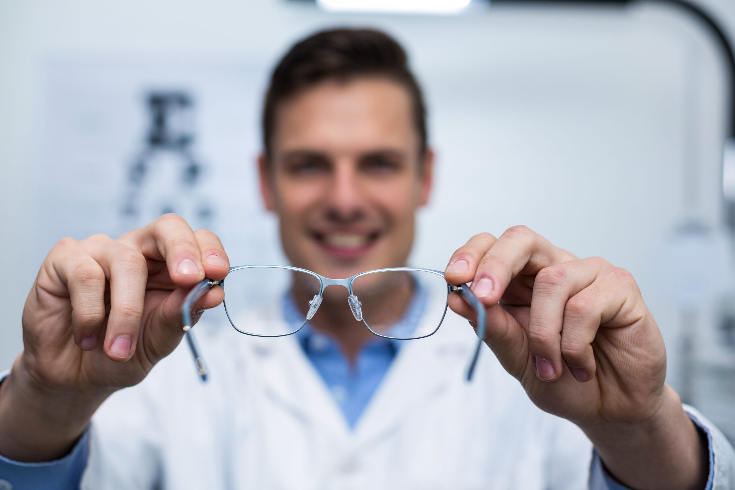 Smiling optometrist holding spectacles in ophthalmology clinic