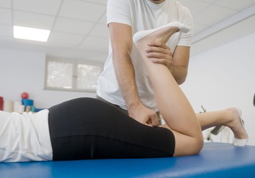 Male physiotherapist standing and doing leg and knee treatment on a female patient in a supine position.