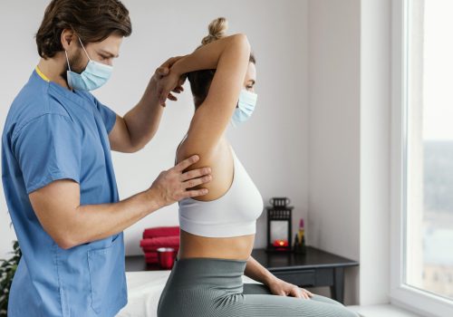 side-male-osteopathic-therapist-with-medical-mask-checking-female-patient-s-shoulder-joint